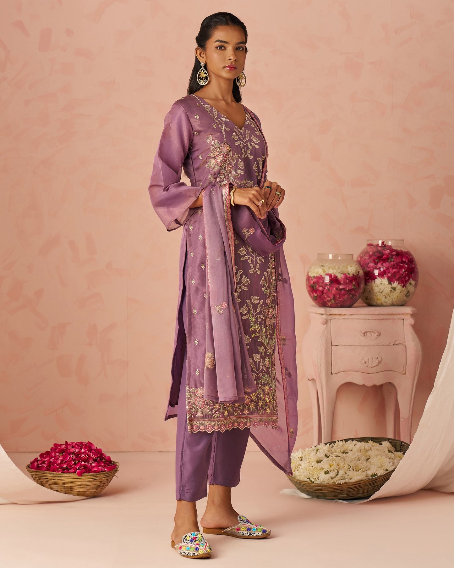 Woman in a purple traditional outfit with floral patterns against a pink background