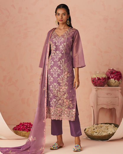 Woman wearing a purple embroidered outfit with a pink background