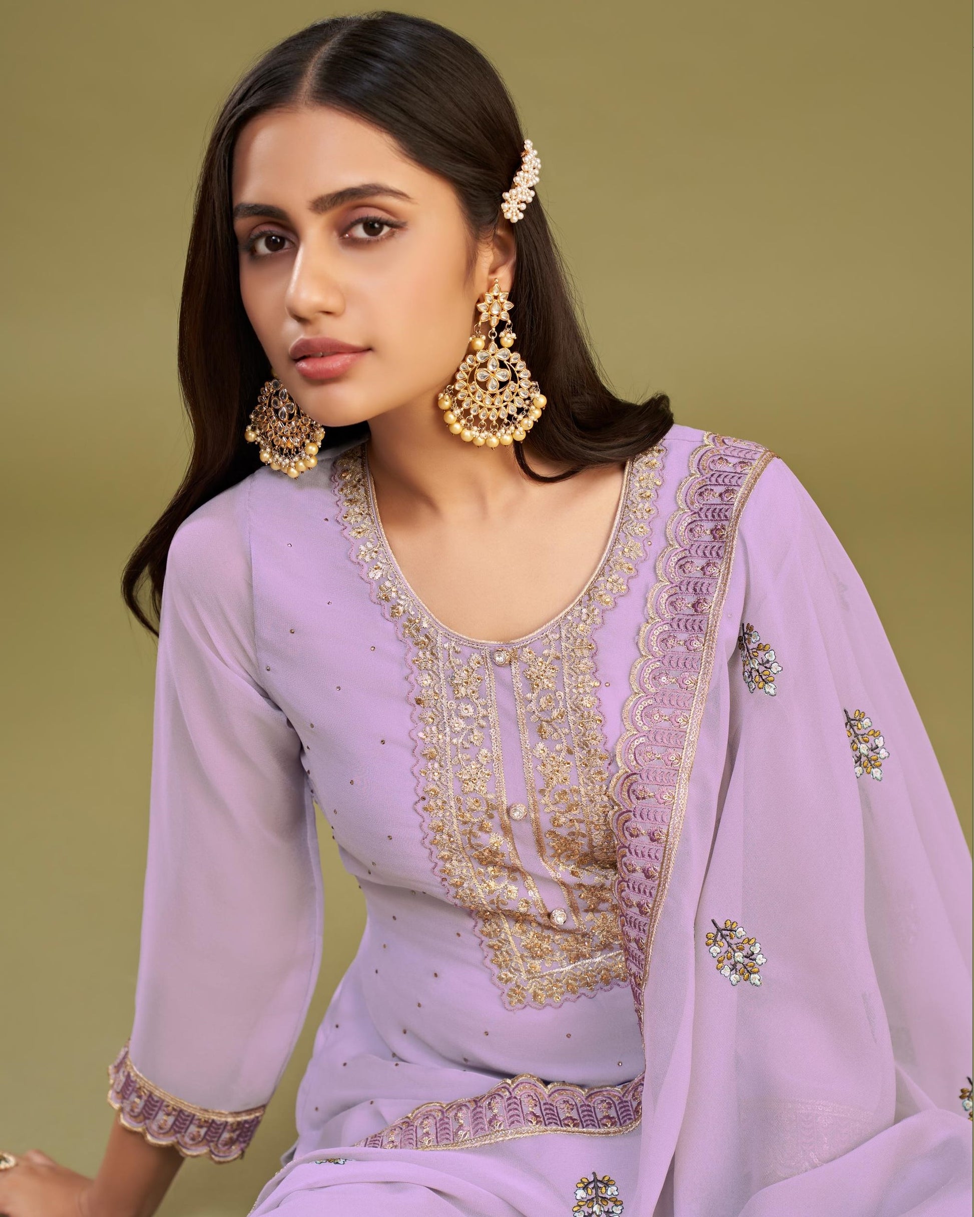 Woman wearing a lavender traditional outfit with gold embroidery against a green background