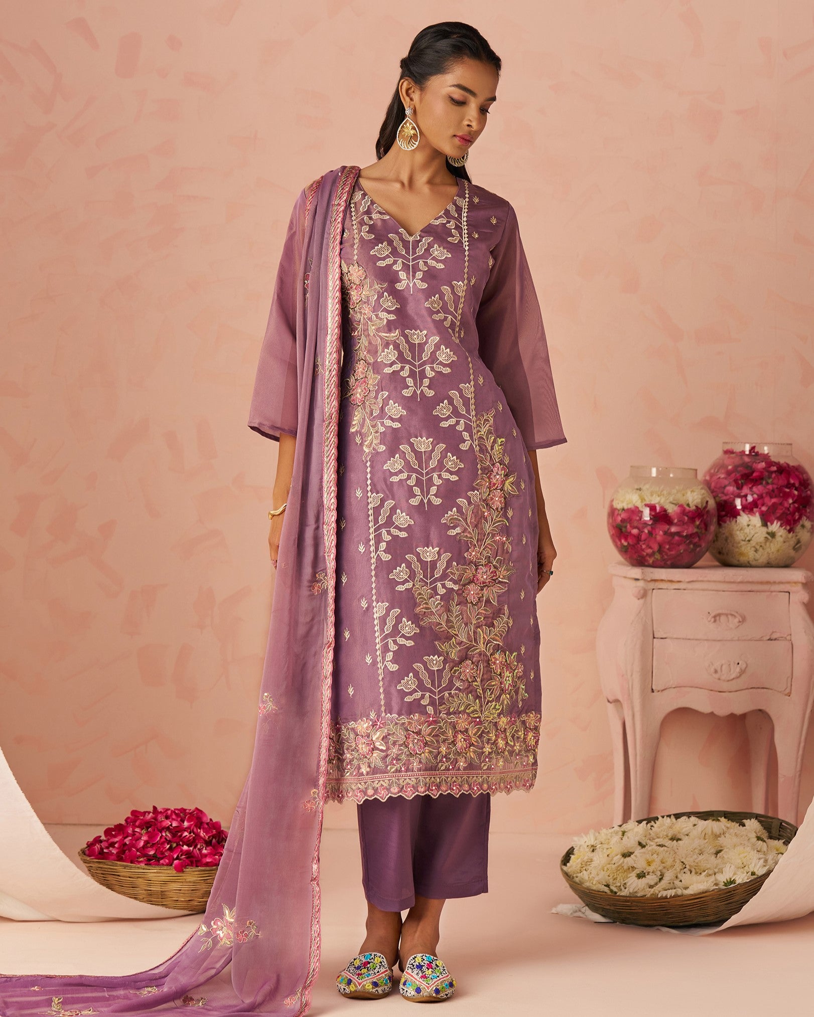 Woman in a traditional outfit with floral patterns against a pink background