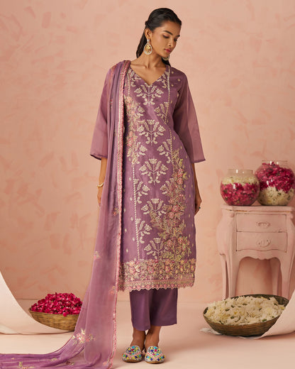 Woman in a traditional outfit with floral patterns against a pink background