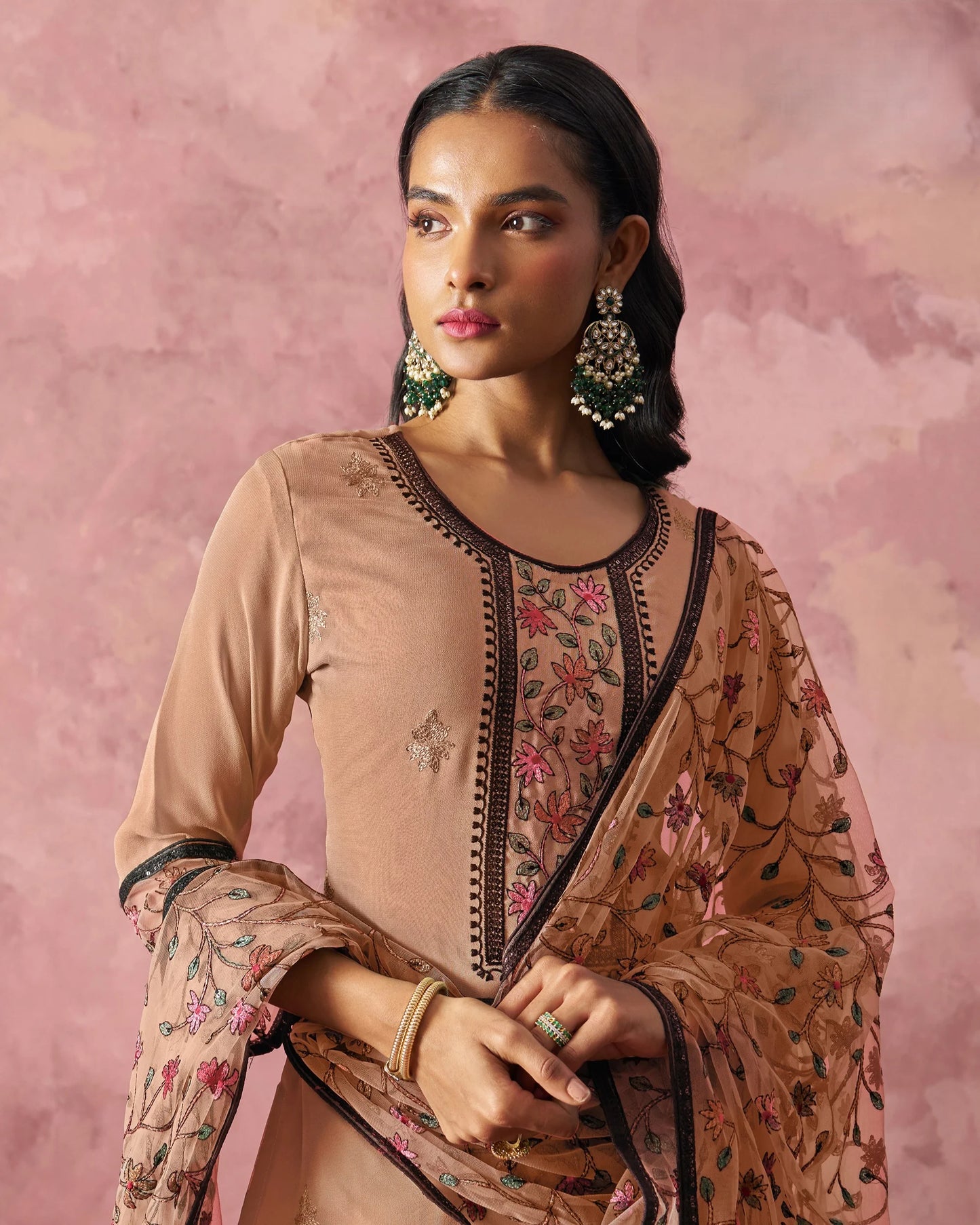 Woman wearing a traditional embroidered outfit with a pink background