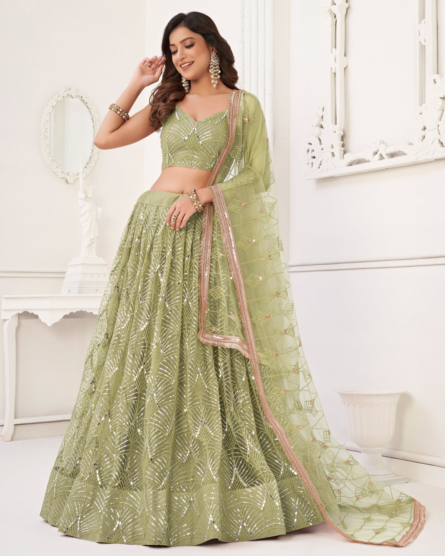 Woman wearing a green embroidered lehenga with a matching blouse in a white decorated room.