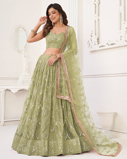 Woman wearing a green embroidered lehenga with a matching blouse in a white decorated room.