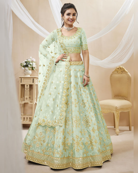 Woman wearing a light green embroidered traditional outfit in a decorated room.