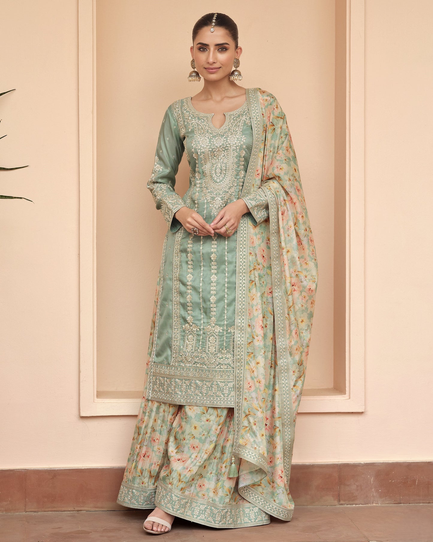 Woman wearing a traditional outfit with a floral pattern against a beige wall.