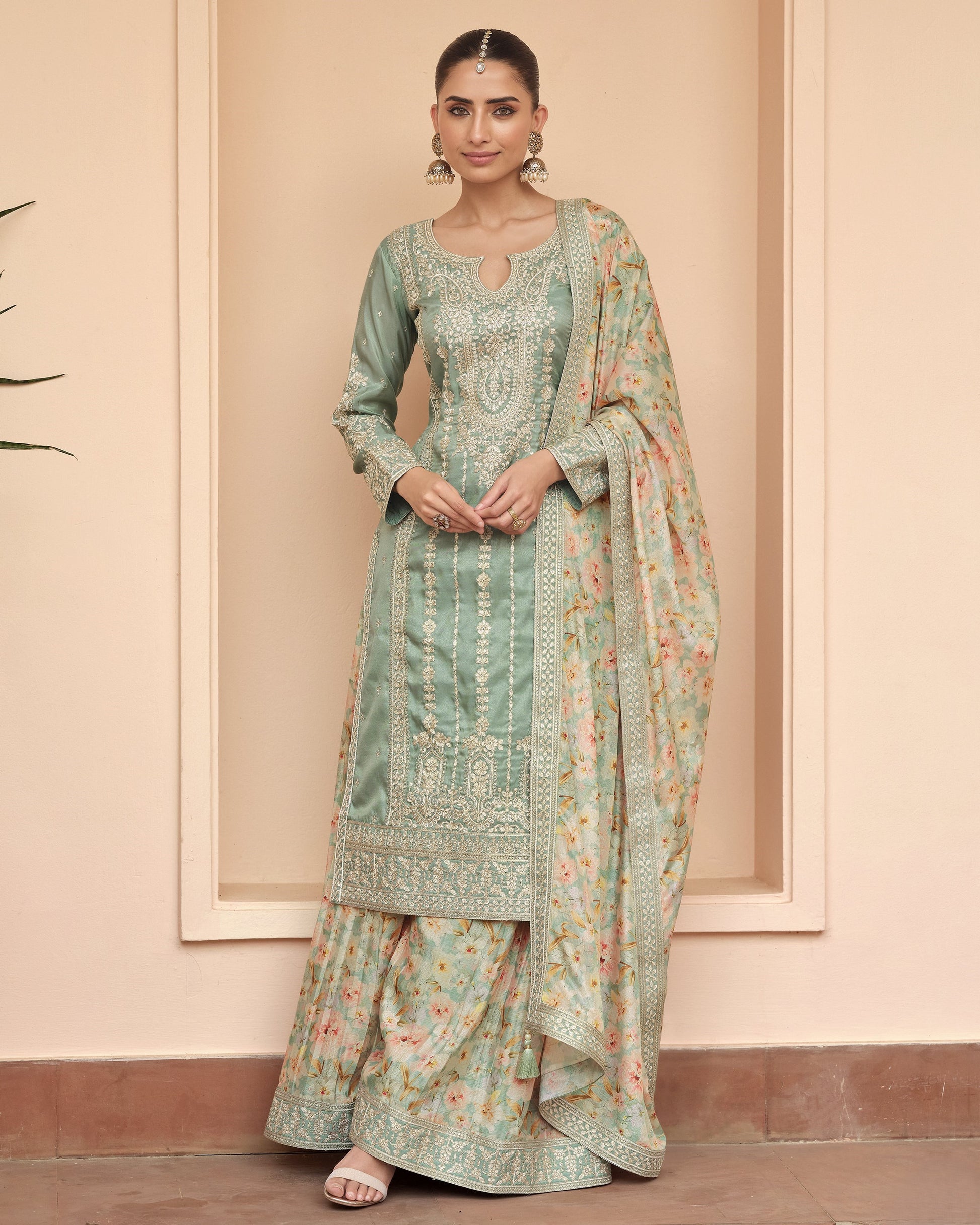 Woman wearing a traditional outfit with a floral pattern against a beige wall.