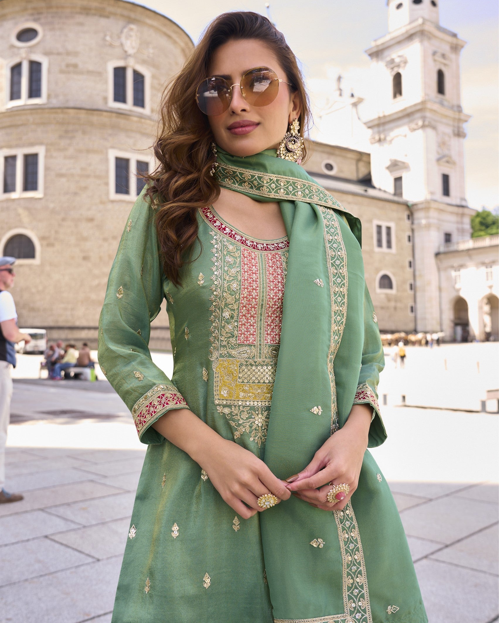 Woman in a green embroidered outfit standing in front of a historic building.
