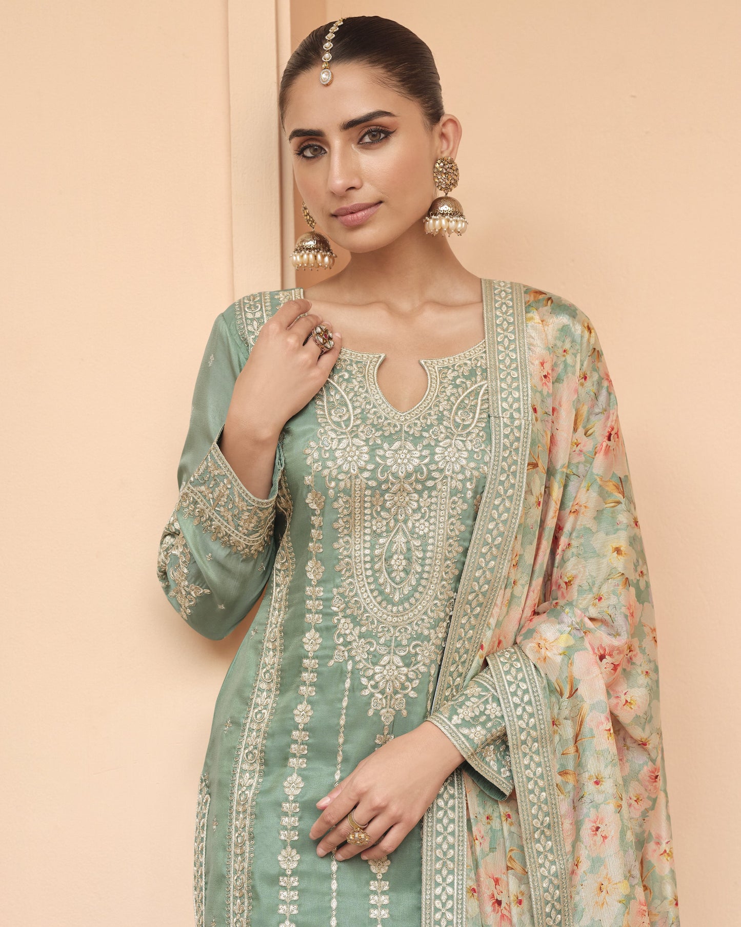 Woman wearing a traditional green embroidered outfit with a floral dupatta against a beige background