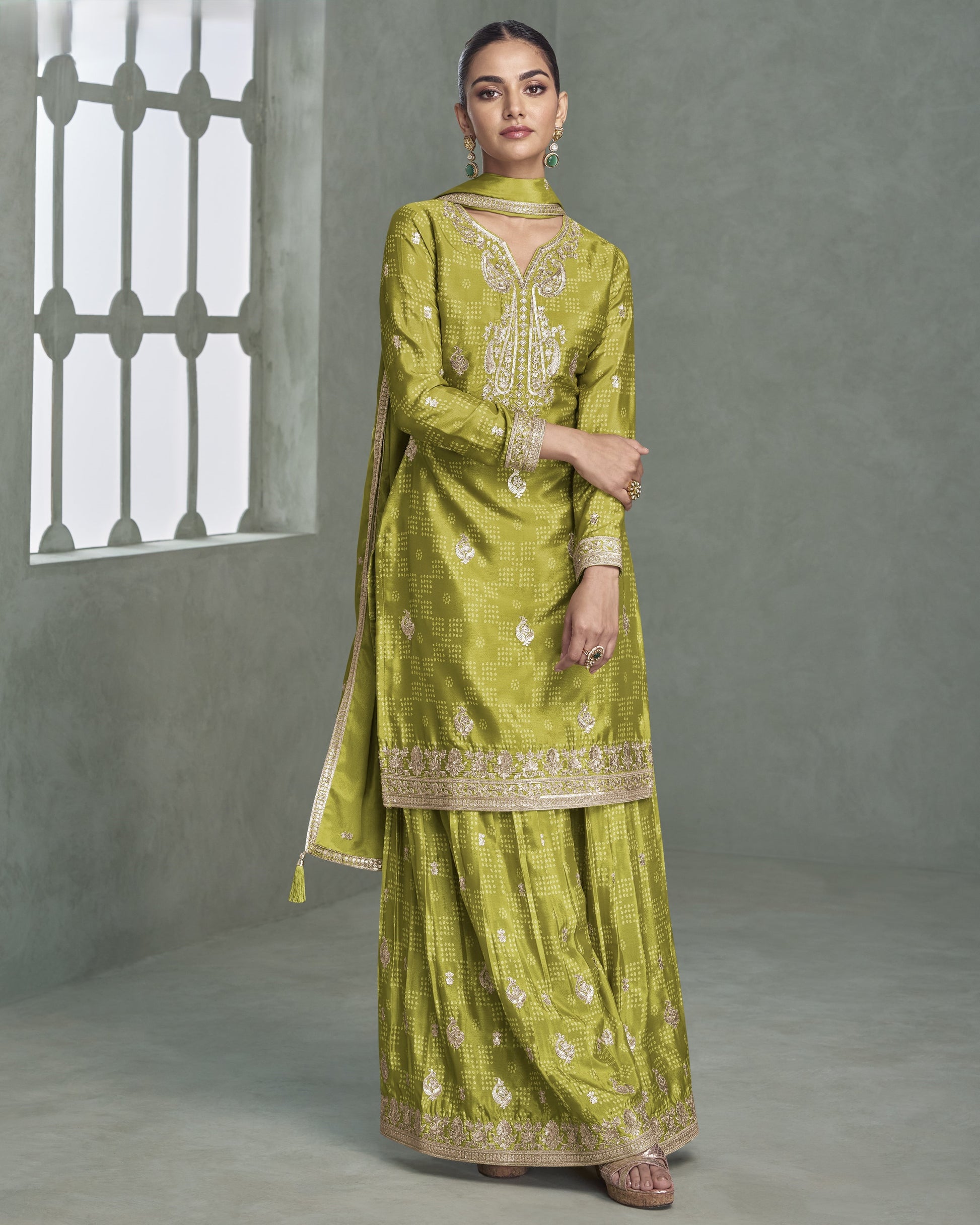 Woman wearing a green traditional outfit with embroidery in a gray room.
