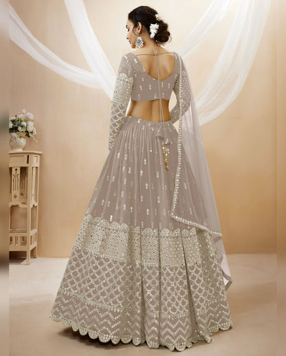 Woman wearing a silver embroidered lehenga with a plain background
