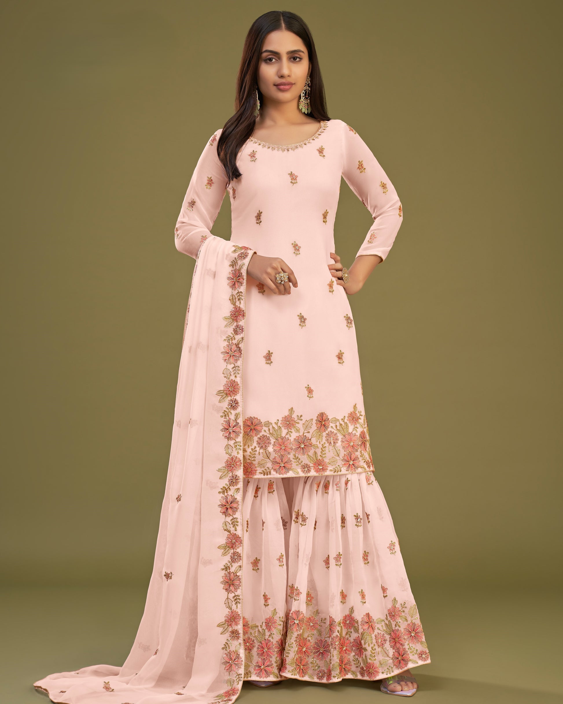 Woman wearing a light pink traditional outfit with floral embroidery on a green background