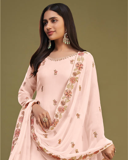 Woman wearing a light pink traditional outfit with floral embroidery on a green background