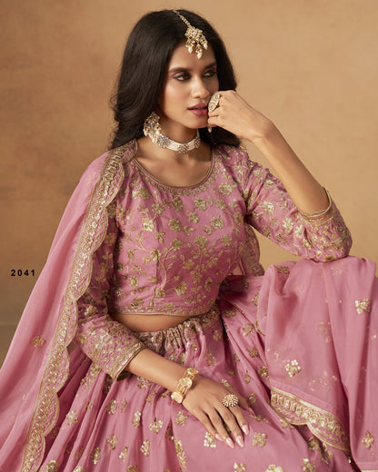 Woman in a pink traditional outfit with gold embroidery against a beige background
