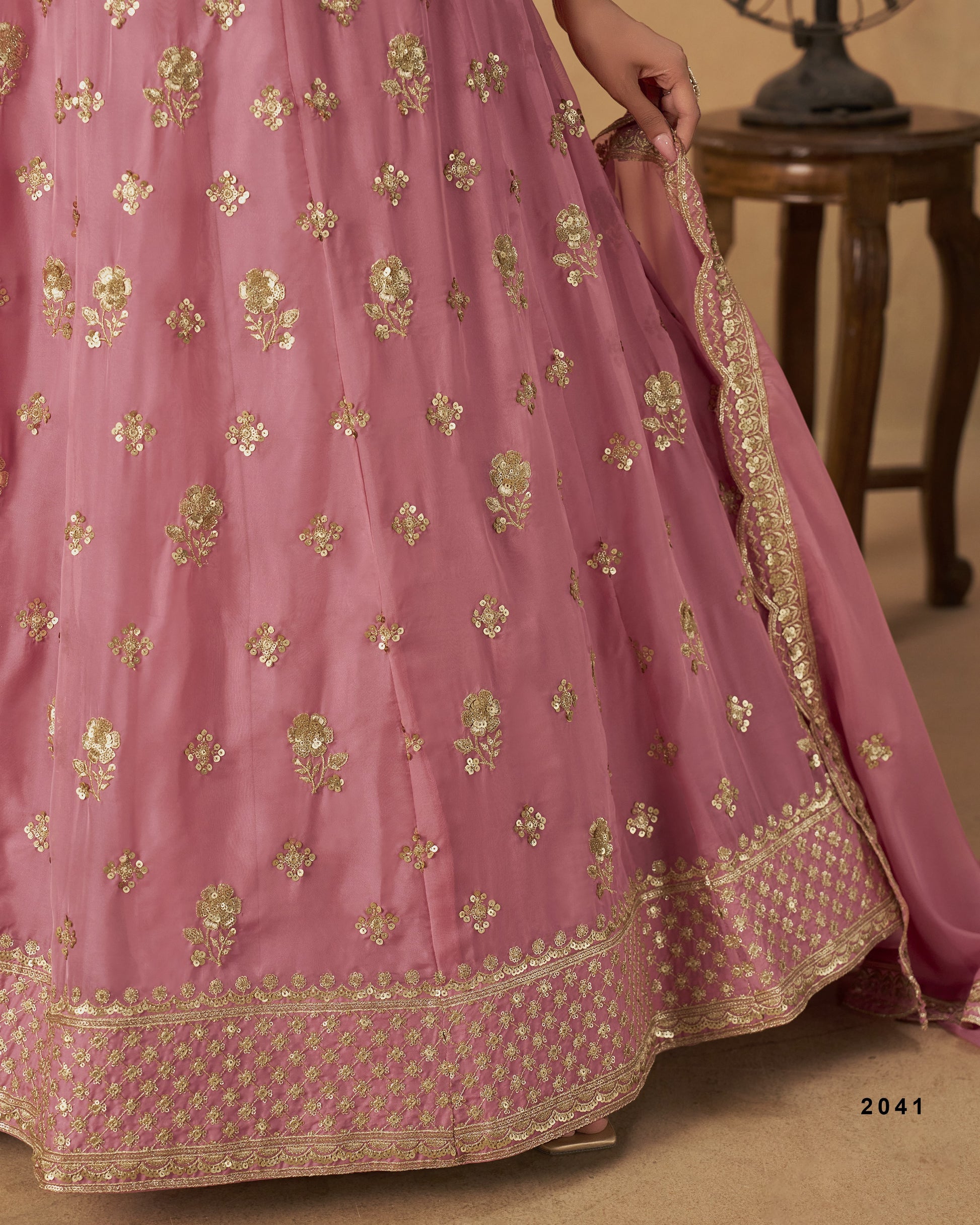 Pink traditional outfit with gold embroidery on a wooden floor.