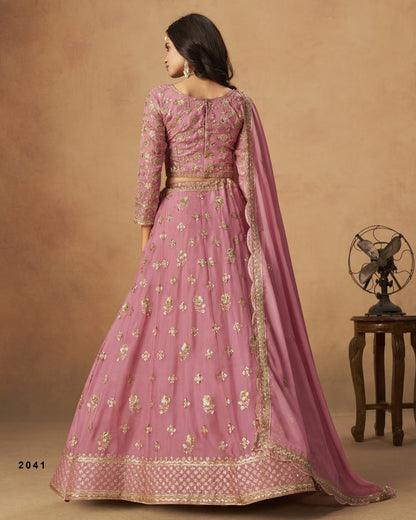 Woman wearing a pink embroidered traditional outfit with a matching dupatta on a brown background