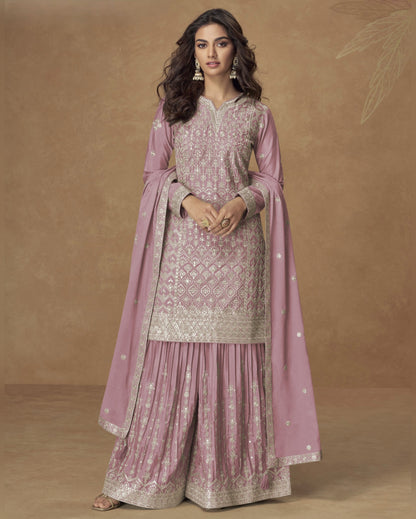 Woman wearing a traditional pink and gold outfit with a matching dupatta against a brown background