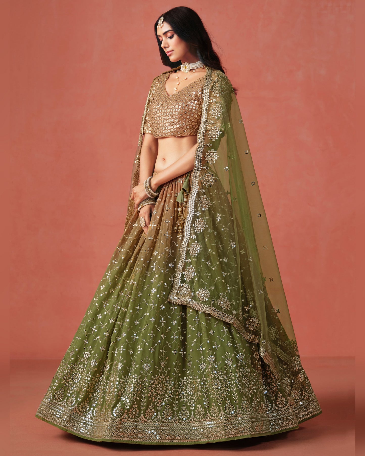 Woman wearing a green and gold traditional outfit with a plain background