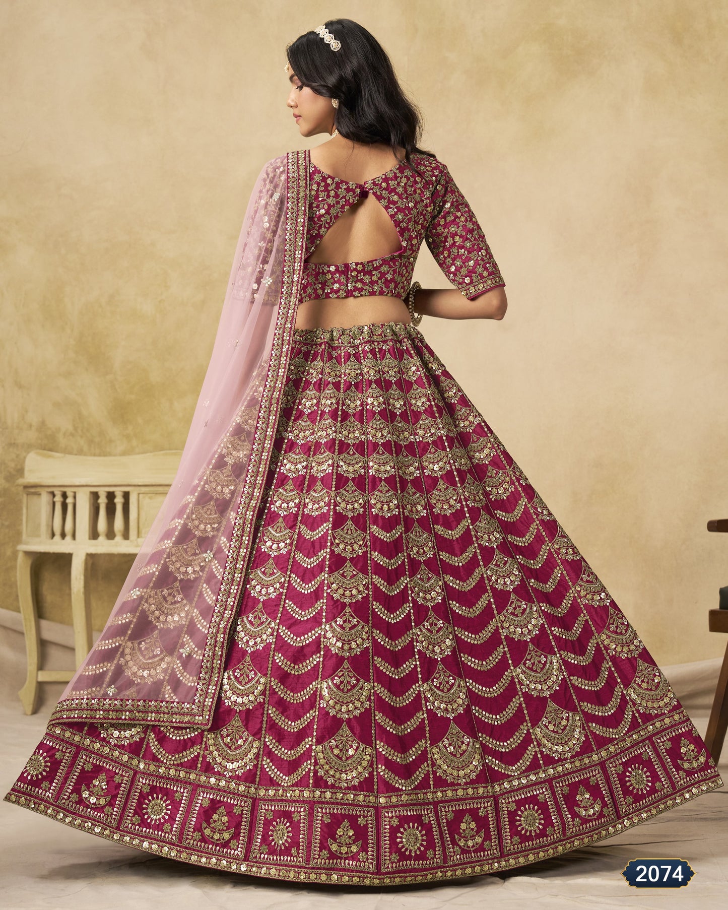 Woman wearing a traditional embroidered pink and red lehenga with a matching dupatta against a beige background.