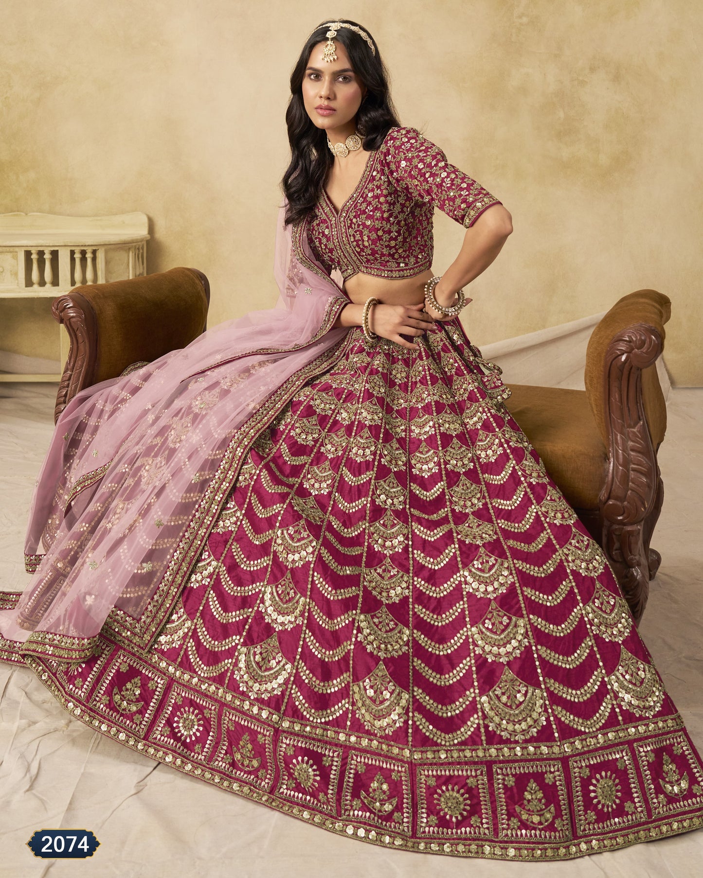 Woman in a traditional pink and red embroidered outfit sitting on a wooden chair.