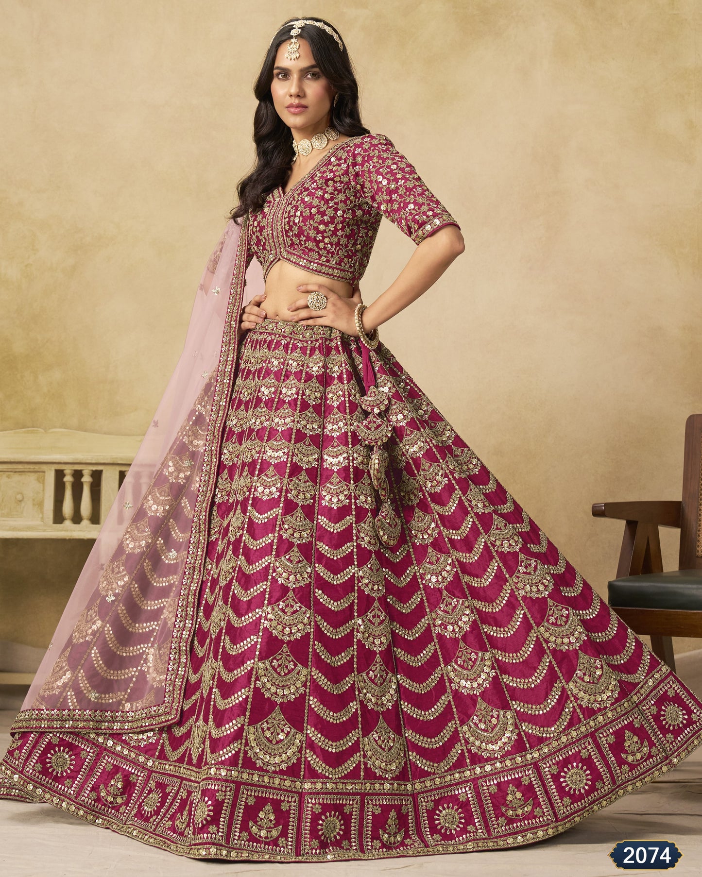 Woman wearing a traditional pink and red embroidered lehenga with a beige background