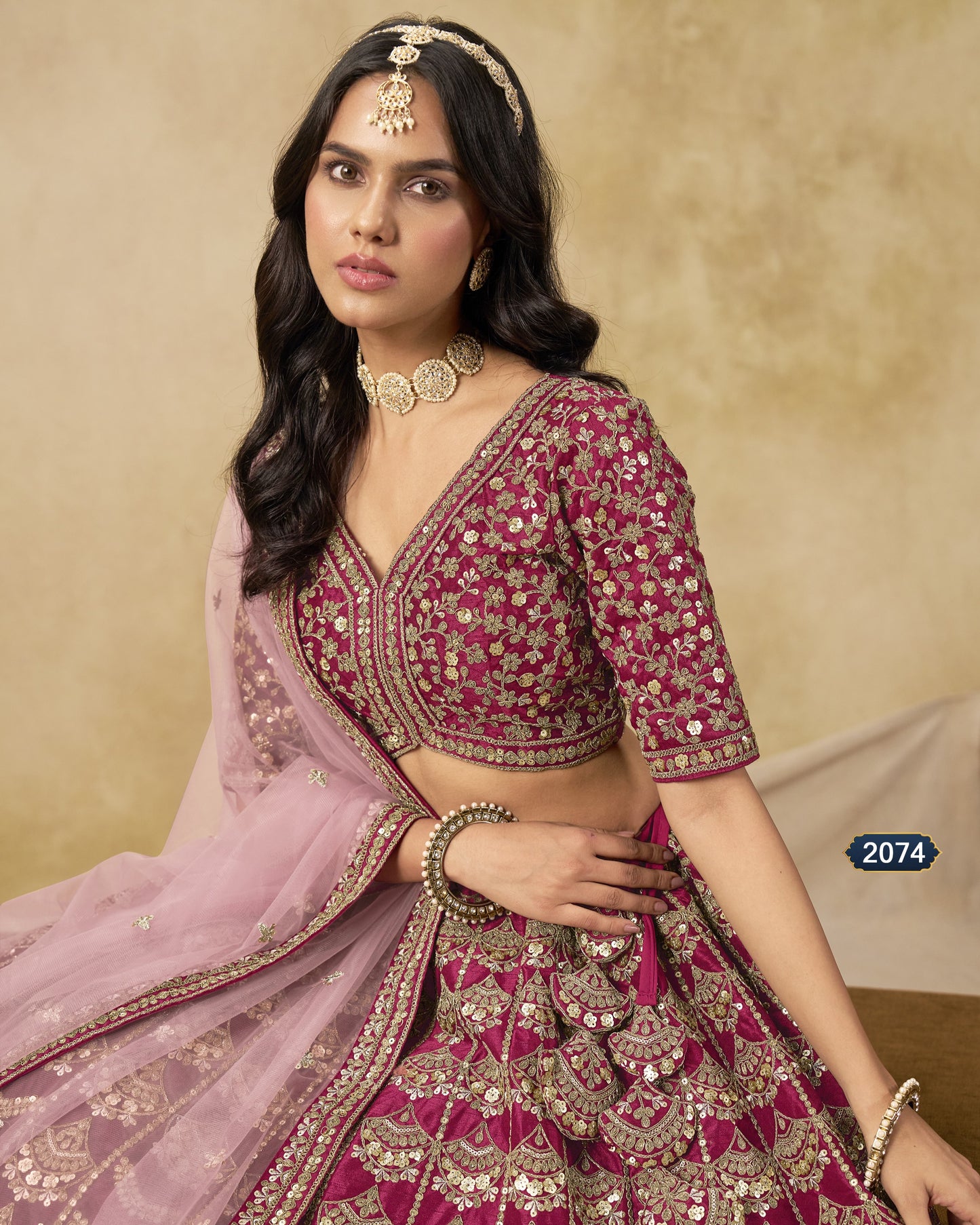 Woman in traditional pink and purple embroidered outfit with jewelry against a beige background