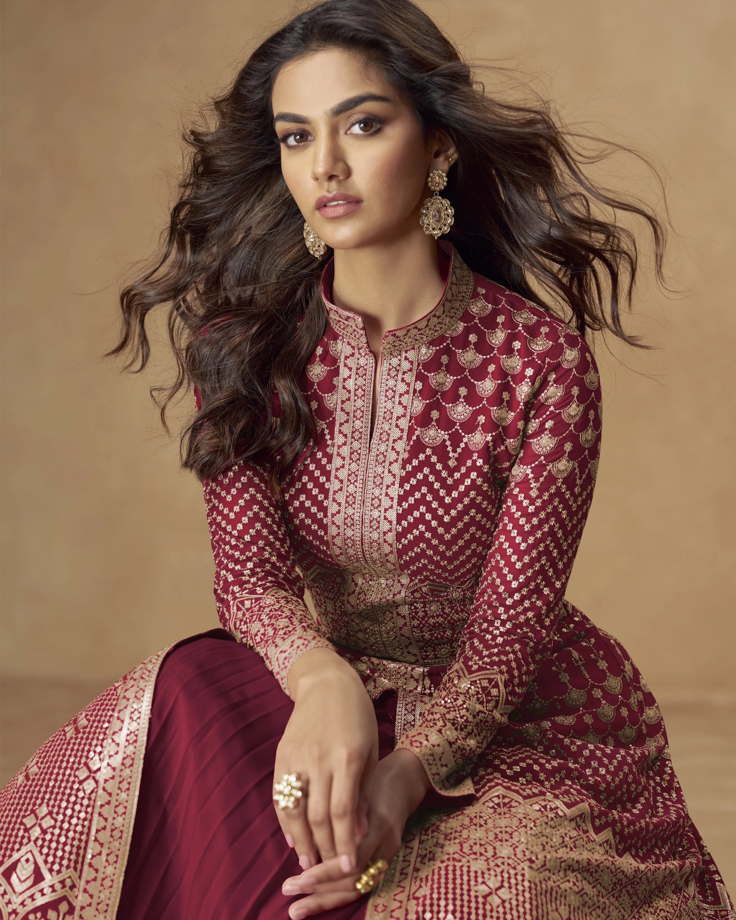 Woman wearing a maroon and gold traditional outfit with jewelry against a beige background