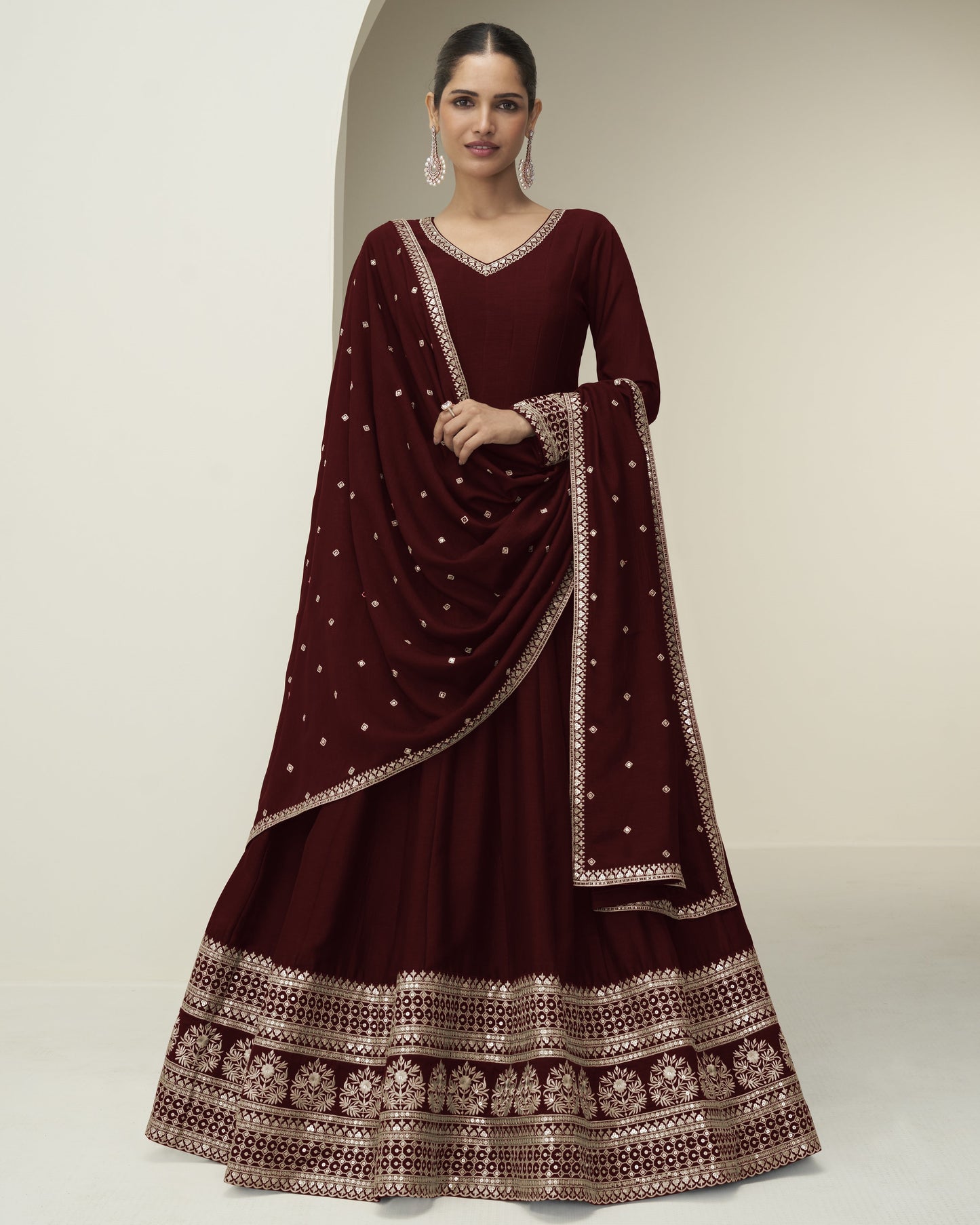 Woman wearing a maroon traditional outfit with intricate patterns on a neutral background