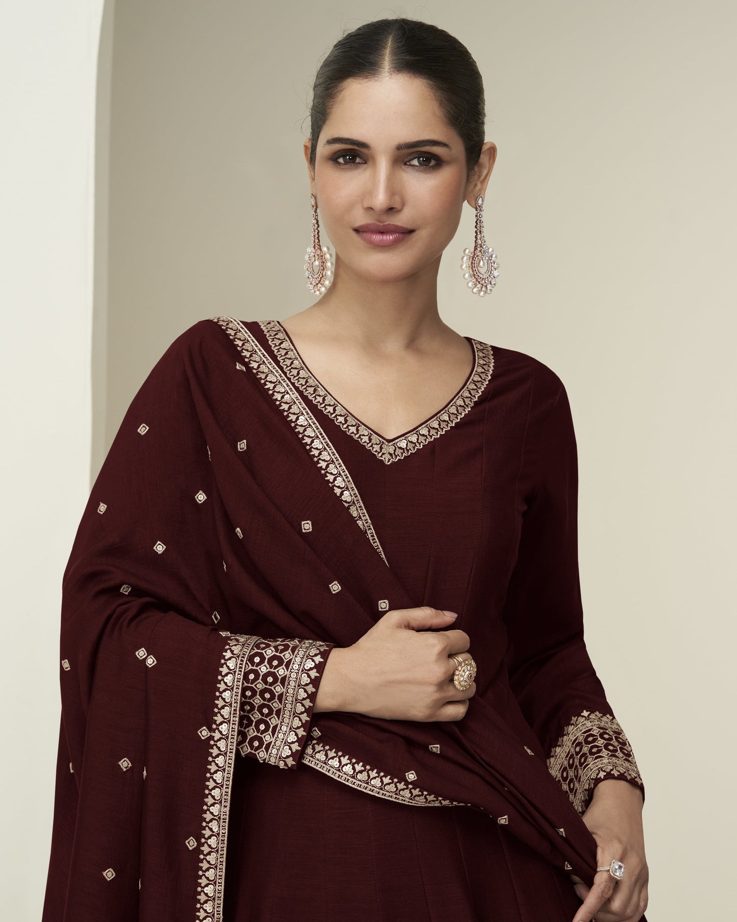 Woman wearing a maroon traditional outfit with intricate patterns on a neutral background
