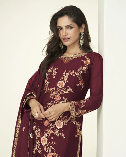 Woman wearing a maroon embroidered traditional outfit against a white background