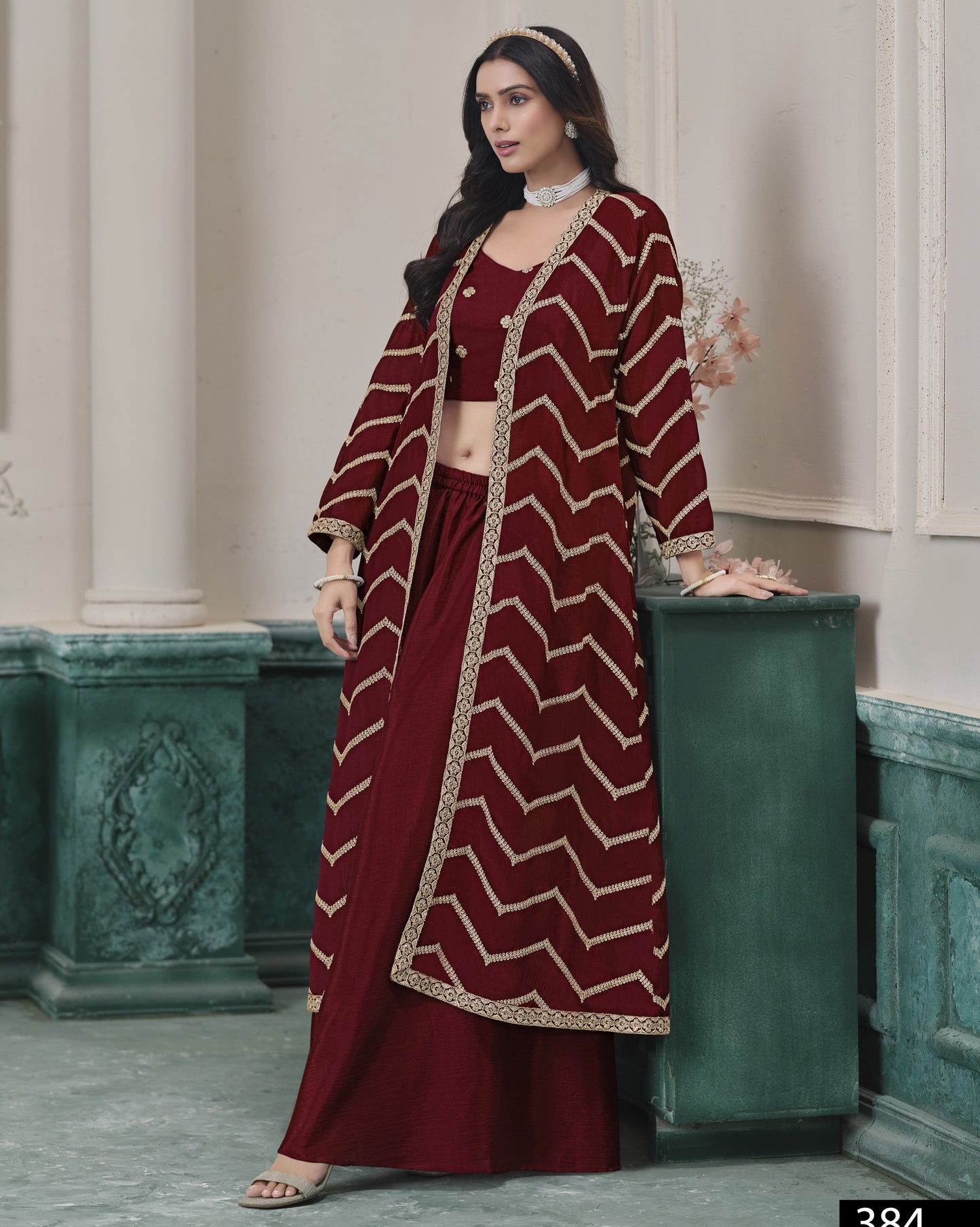 Woman wearing a maroon and gold traditional outfit with a chevron pattern in an elegant indoor setting.