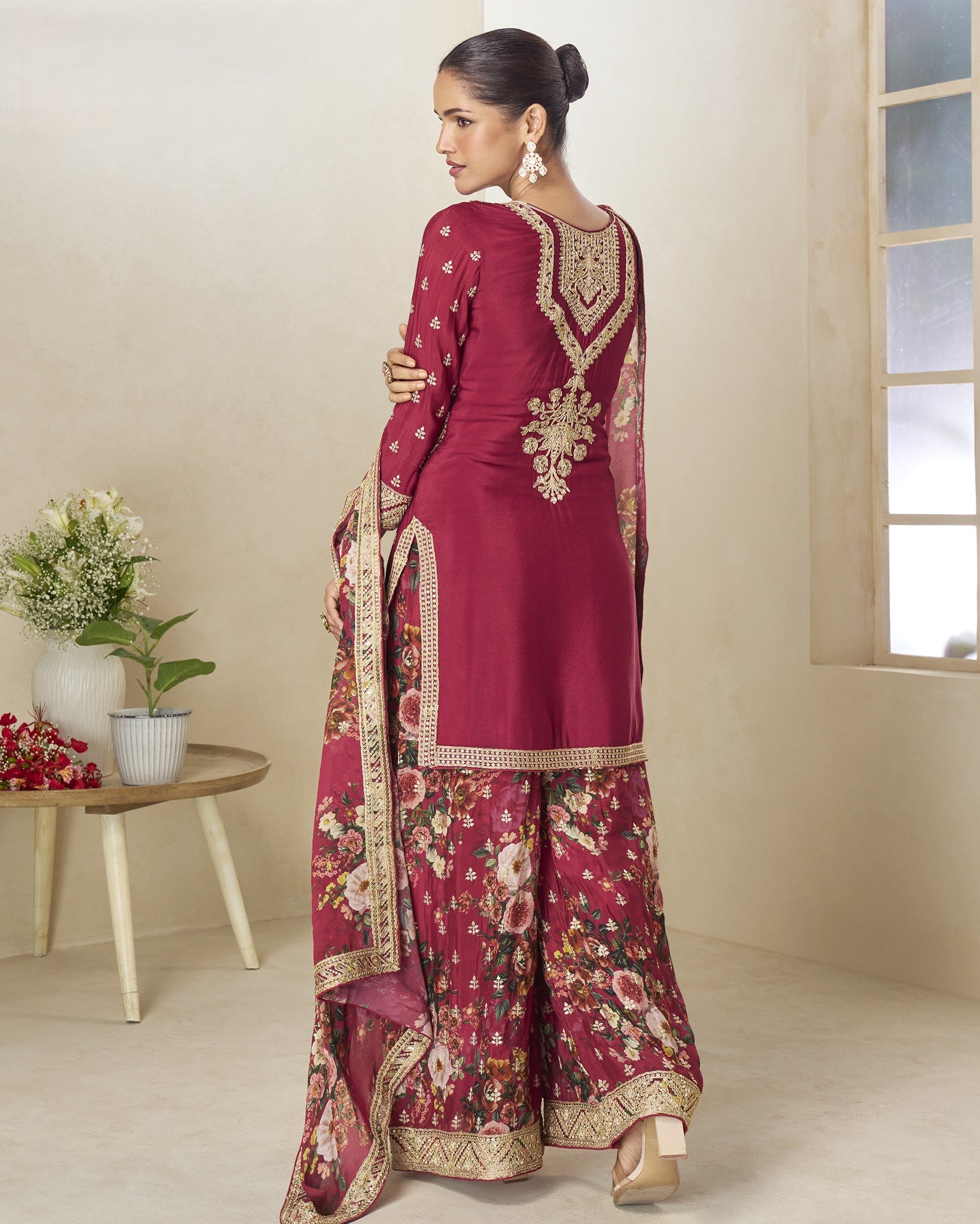Woman in a maroon traditional outfit with floral patterns in a room.