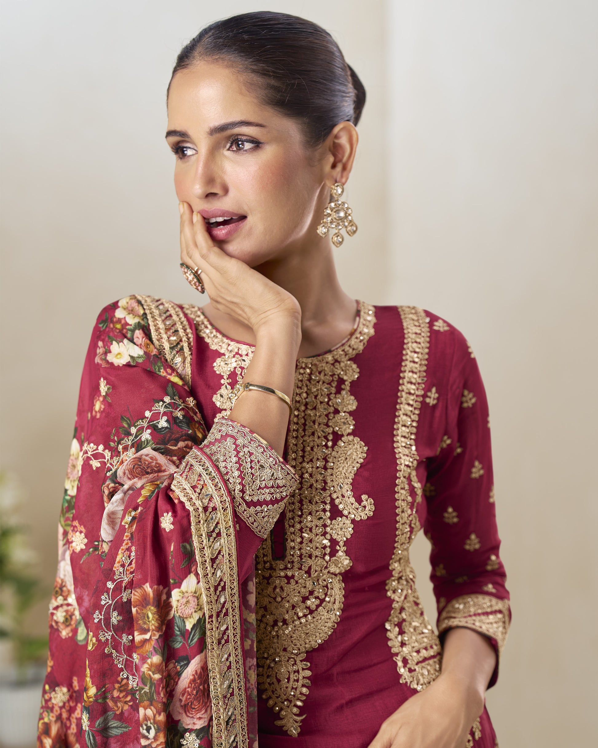 Woman wearing a maroon traditional outfit with gold embroidery and floral patterns.