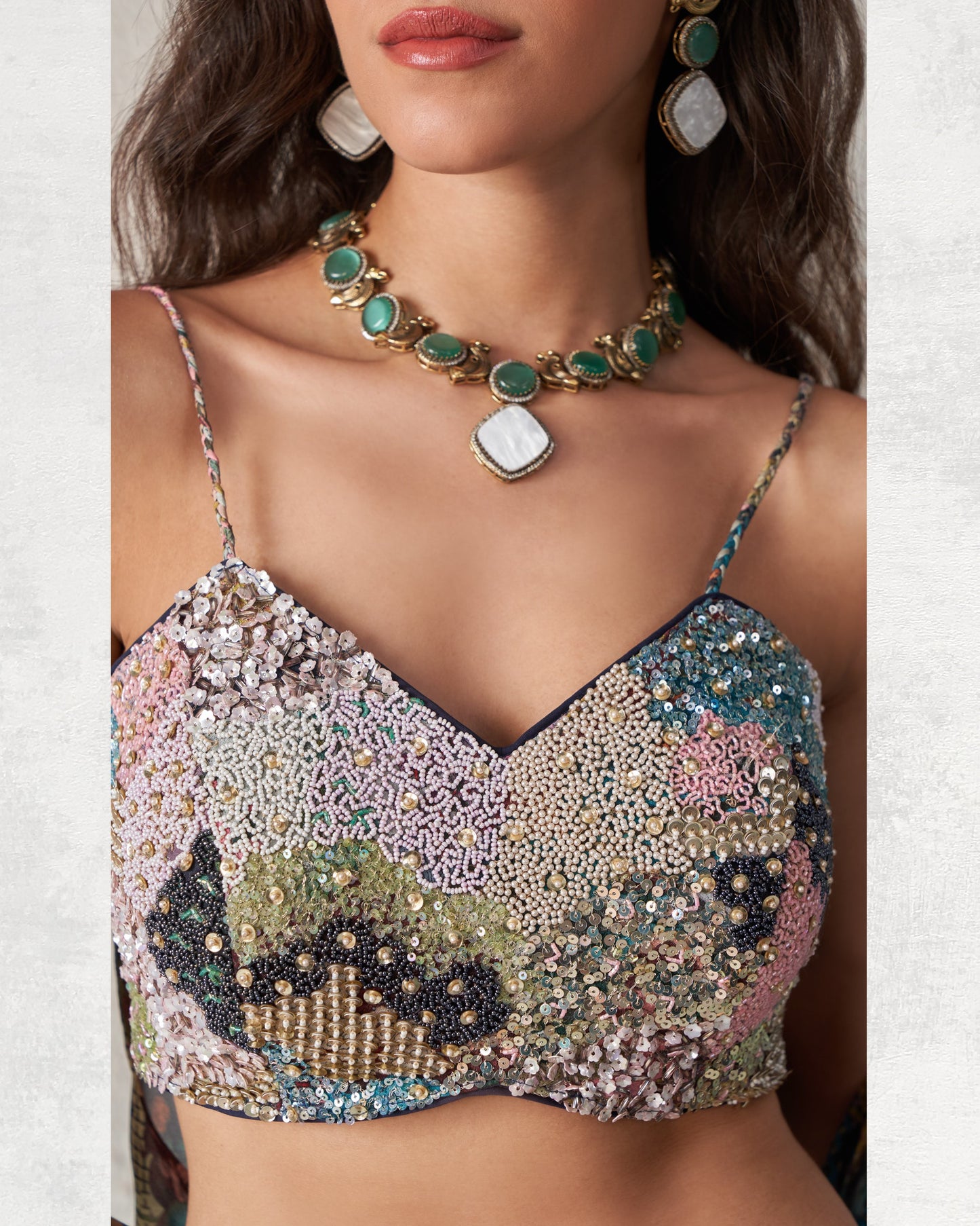 Multicolored beaded top worn by a model with jewelry on a neutral background
