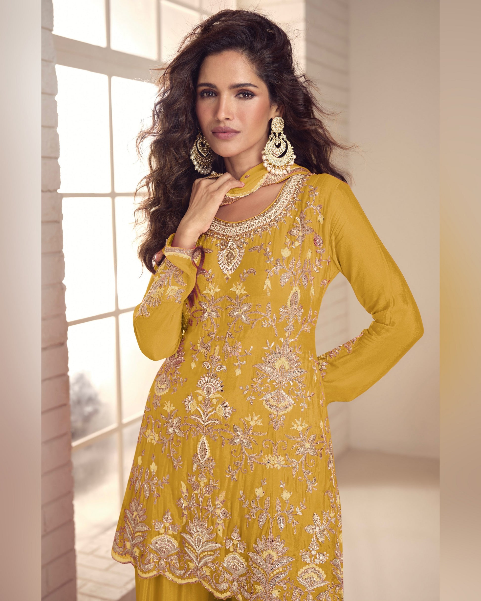 Woman wearing a yellow embroidered dress with intricate patterns indoors.