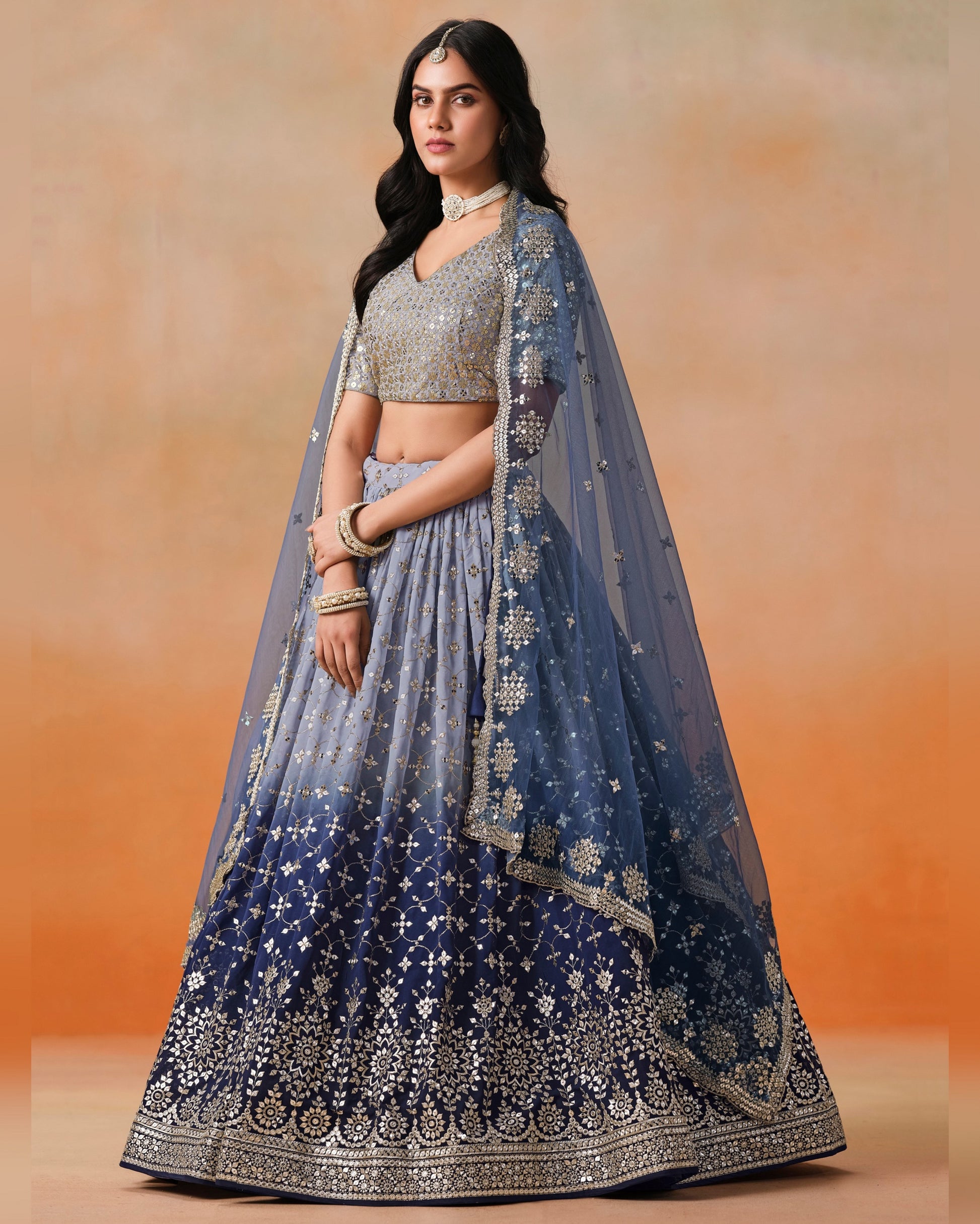 Woman wearing a blue embroidered lehenga with a plain background