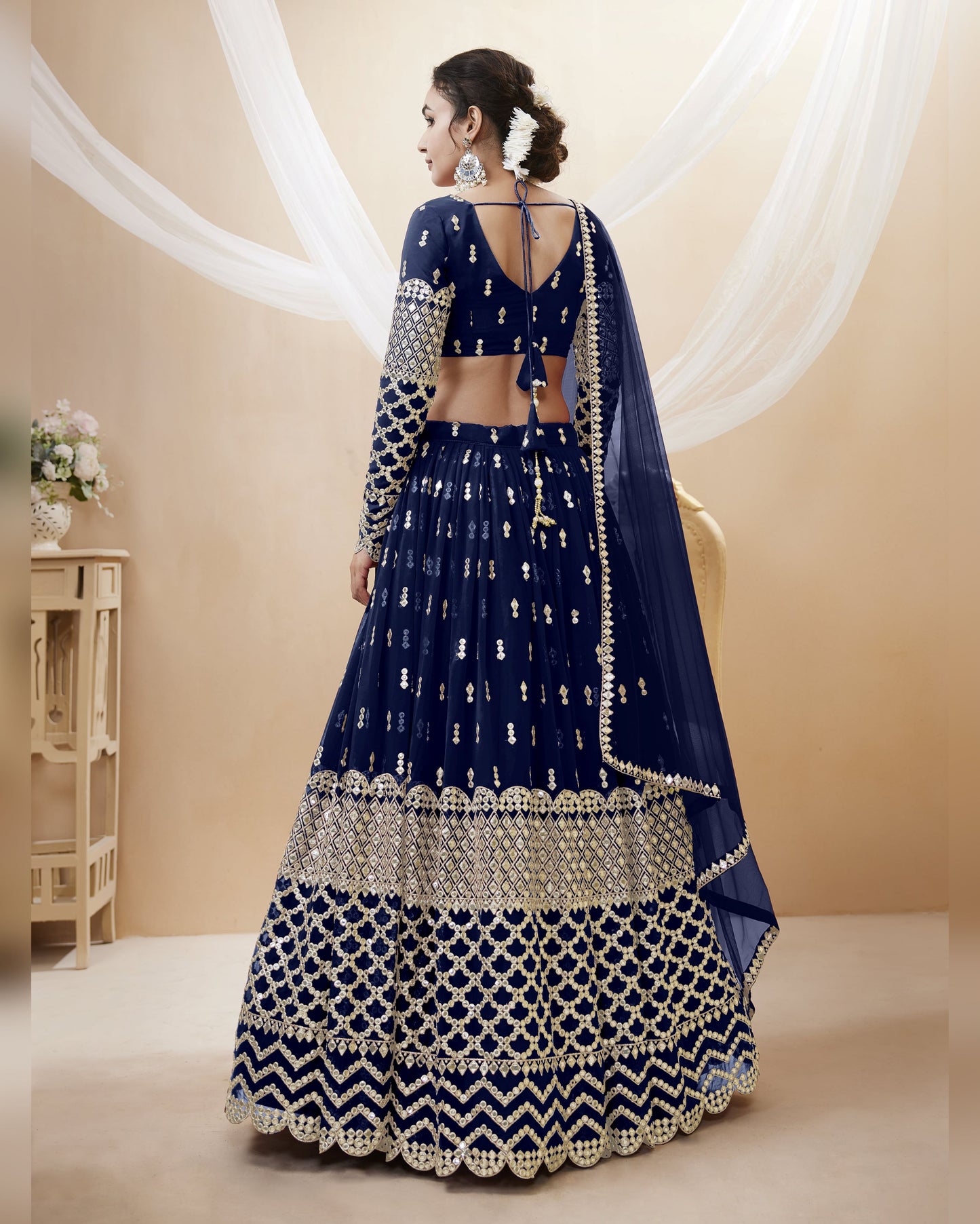 Woman wearing a blue and silver embroidered traditional outfit in a beige room.