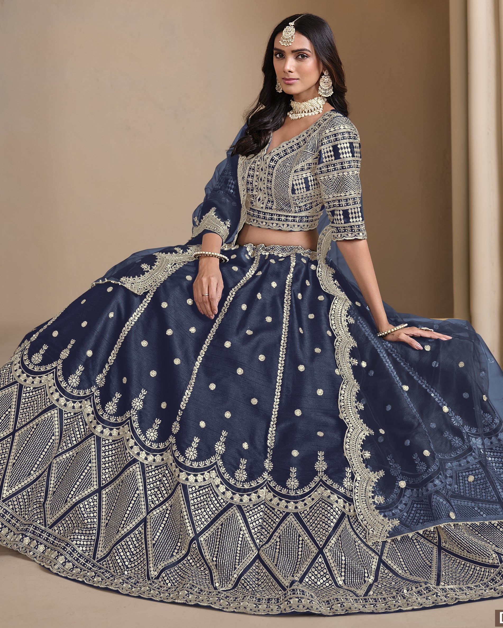 Woman wearing a navy blue embroidered lehenga with silver details on a beige background