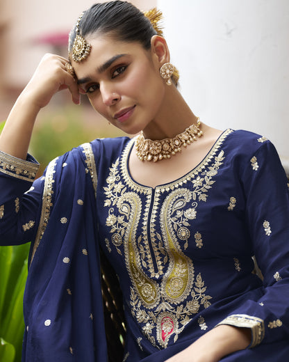Woman wearing a blue embroidered traditional outfit with gold jewelry against a blurred background