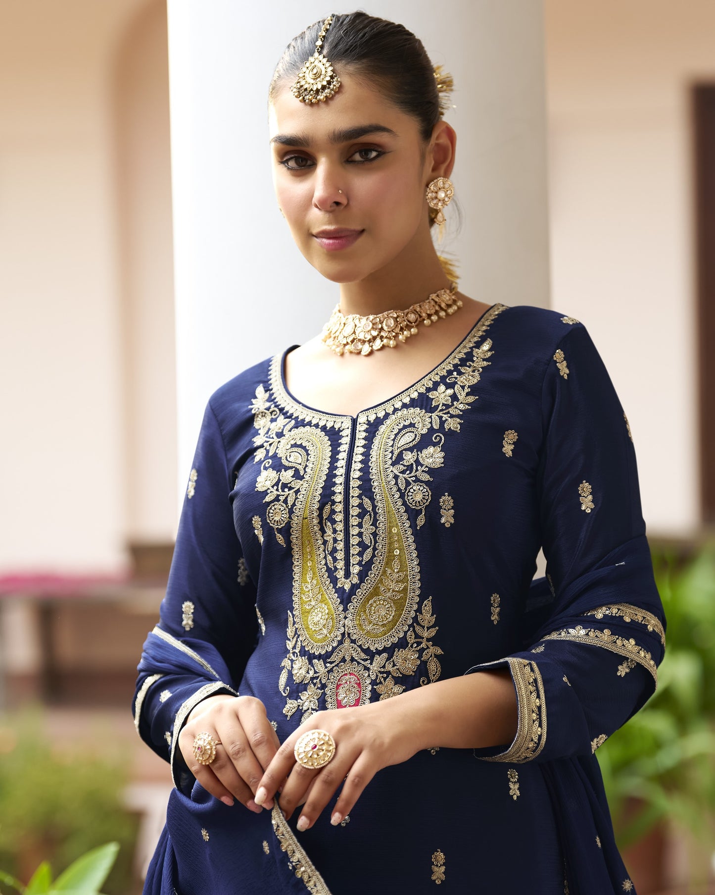 Woman wearing a navy blue embroidered outfit with gold jewelry indoors.
