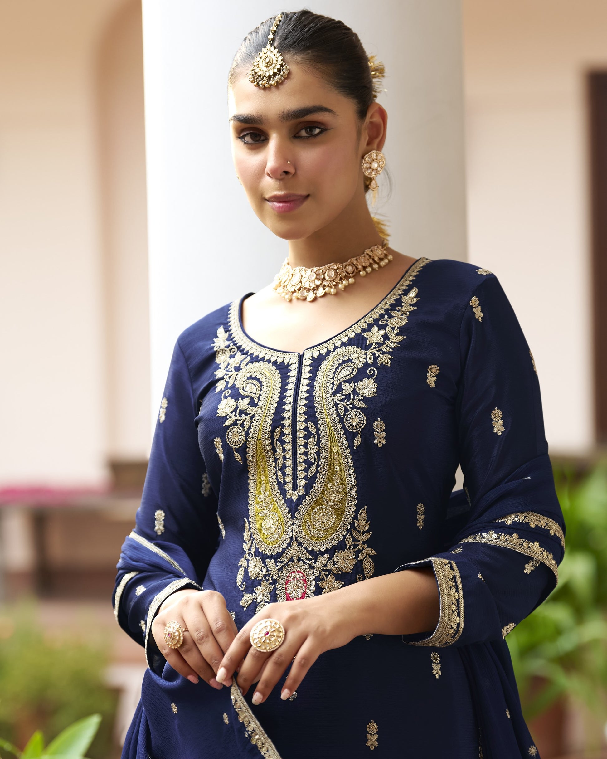 Woman wearing a navy blue embroidered outfit with gold jewelry indoors.
