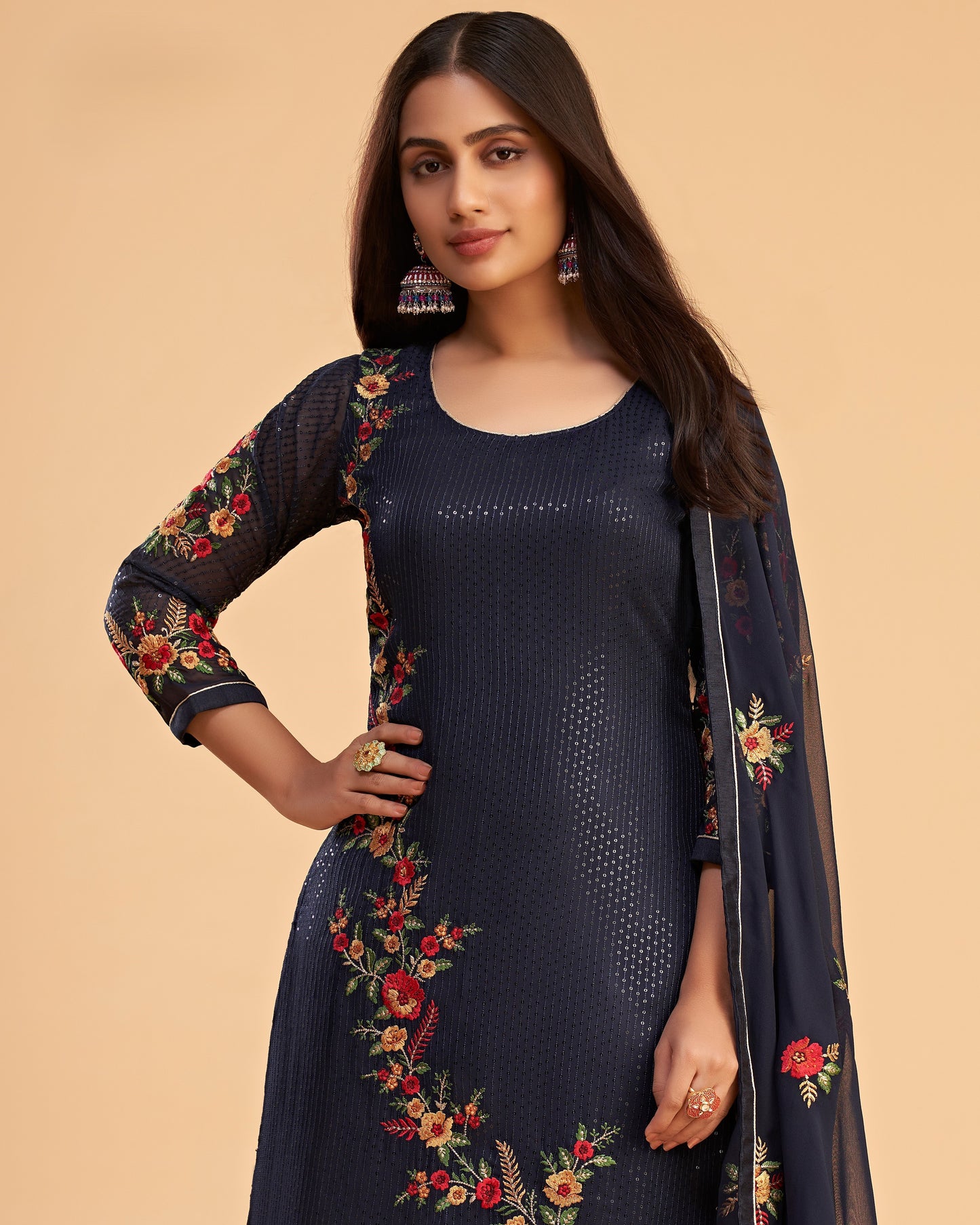 Woman wearing a navy blue dress with floral embroidery on a beige background