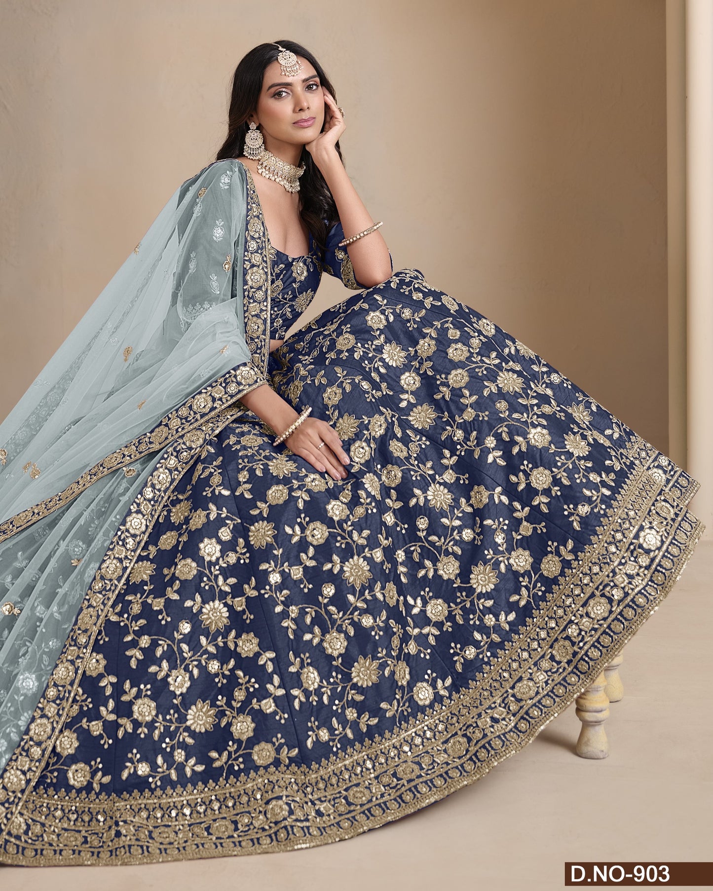 Woman in a traditional blue and gold embroidered outfit with a light blue dupatta on a beige background