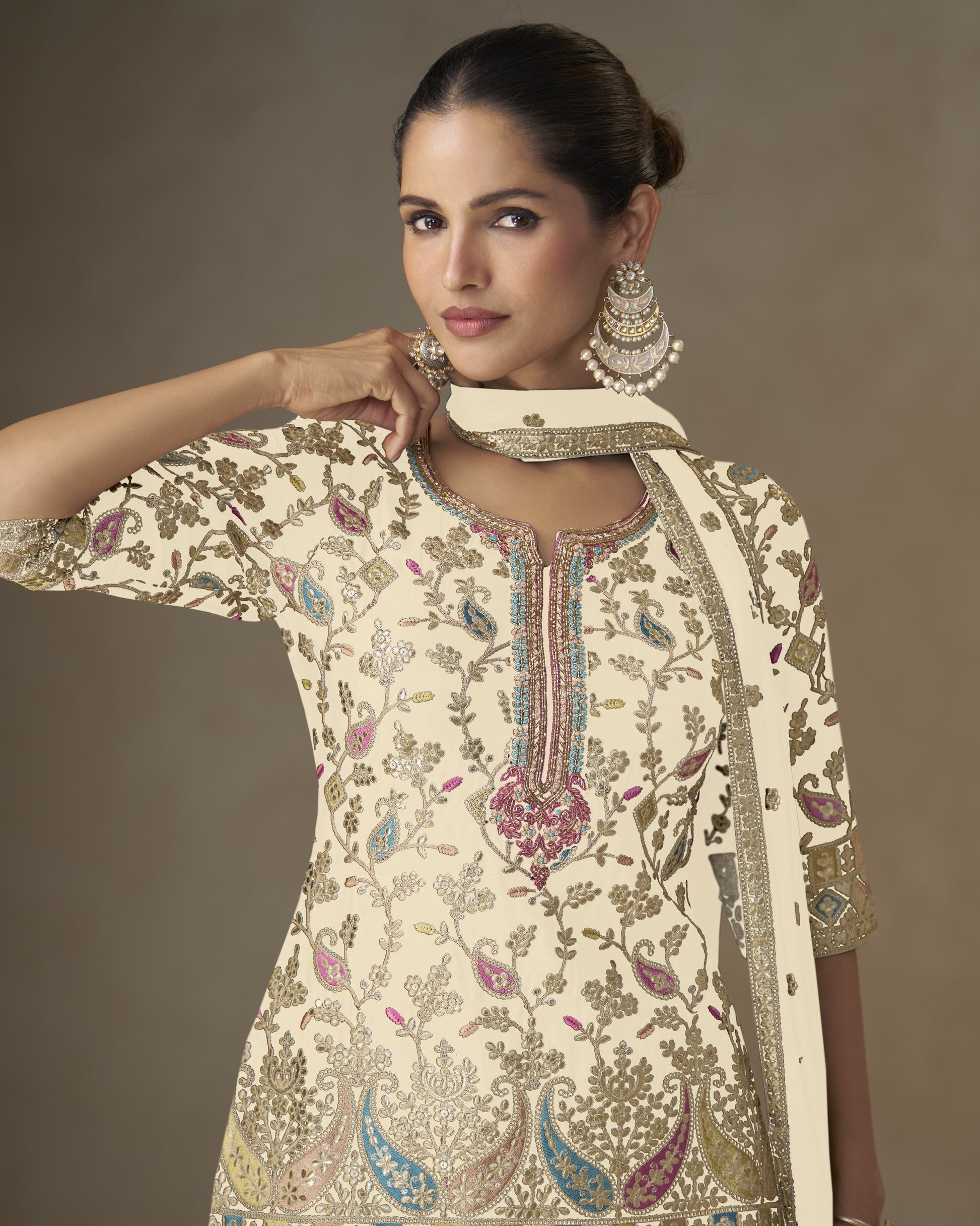 Woman wearing a cream embroidered traditional outfit with a brown background