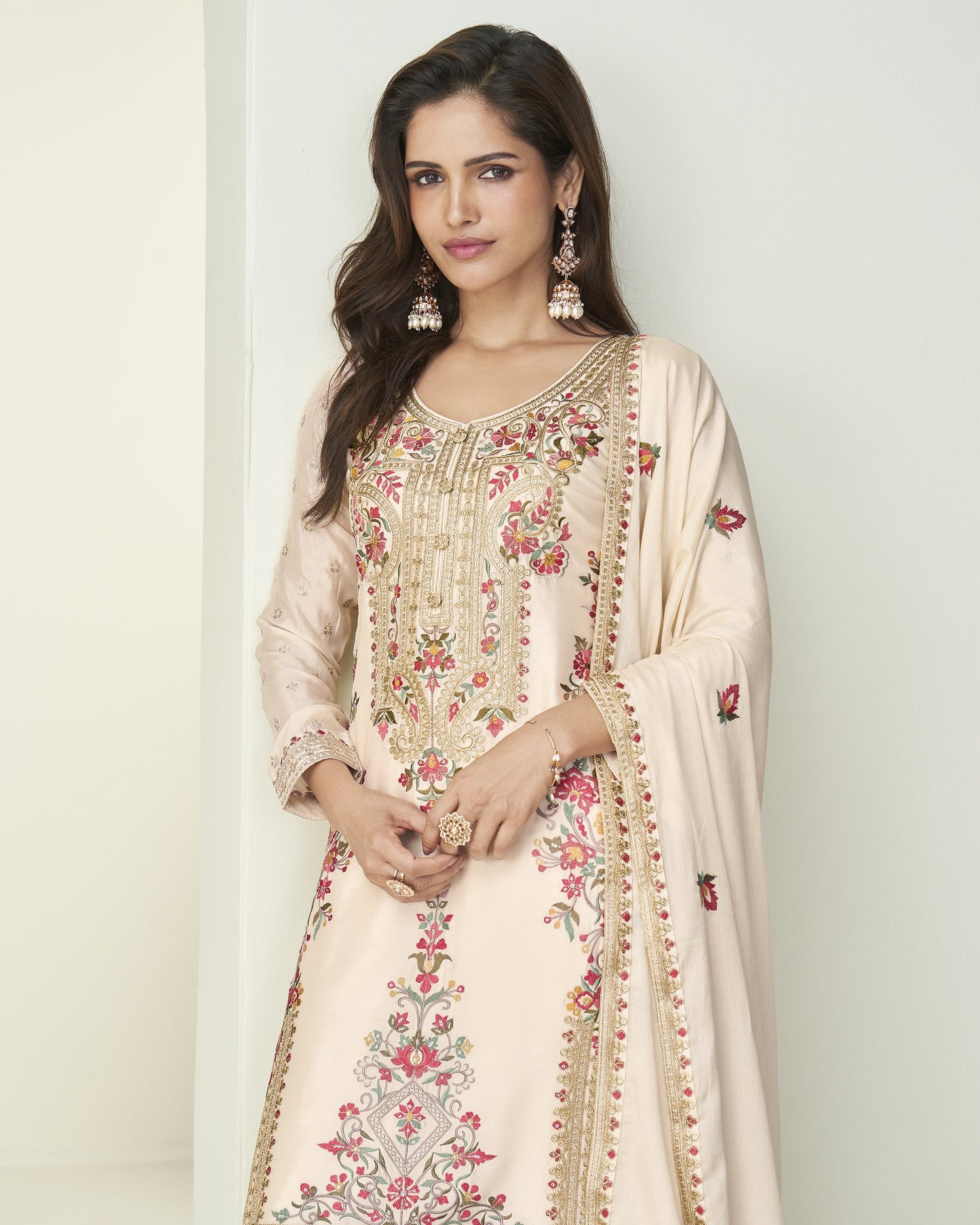 Woman wearing a cream-colored embroidered traditional outfit with a plain background