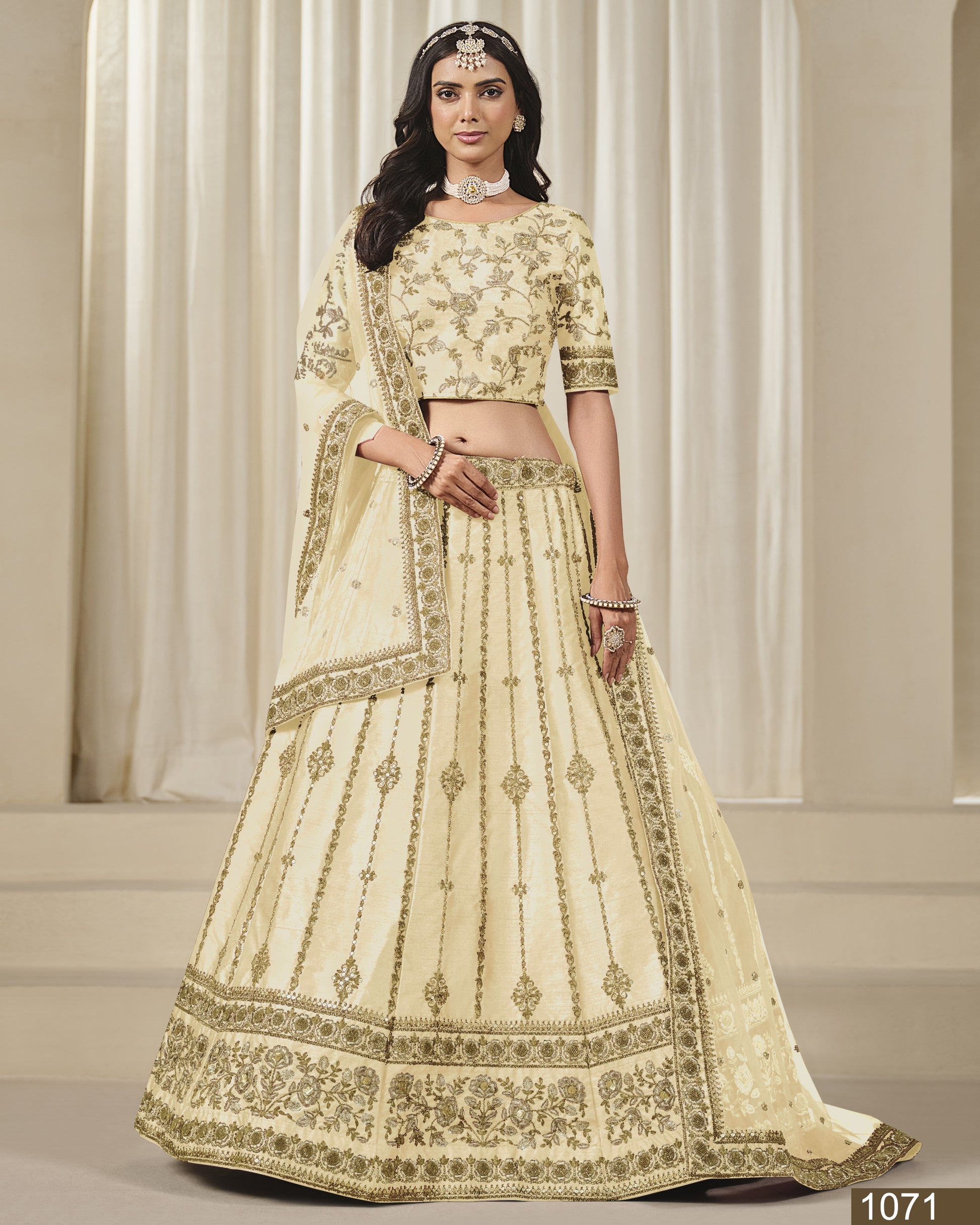 Woman wearing a cream-colored embroidered lehenga with gold details against a neutral background
