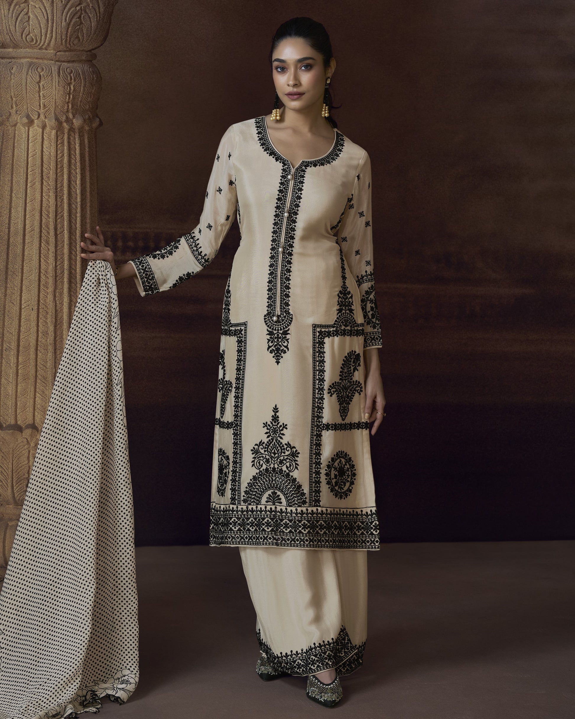 Woman wearing a cream embroidered outfit against a dark background