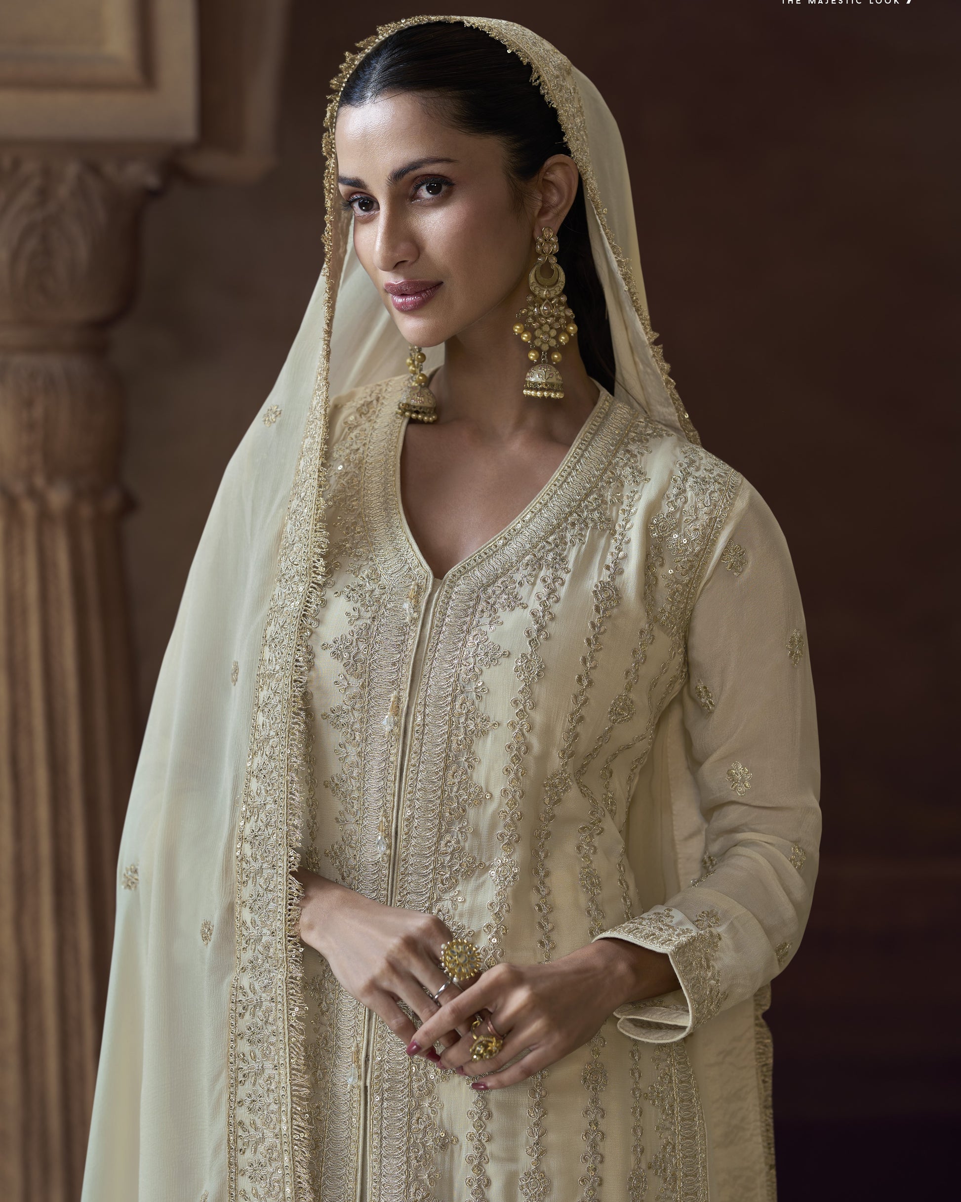 Woman in traditional embroidered outfit with gold jewelry against a warm-toned background