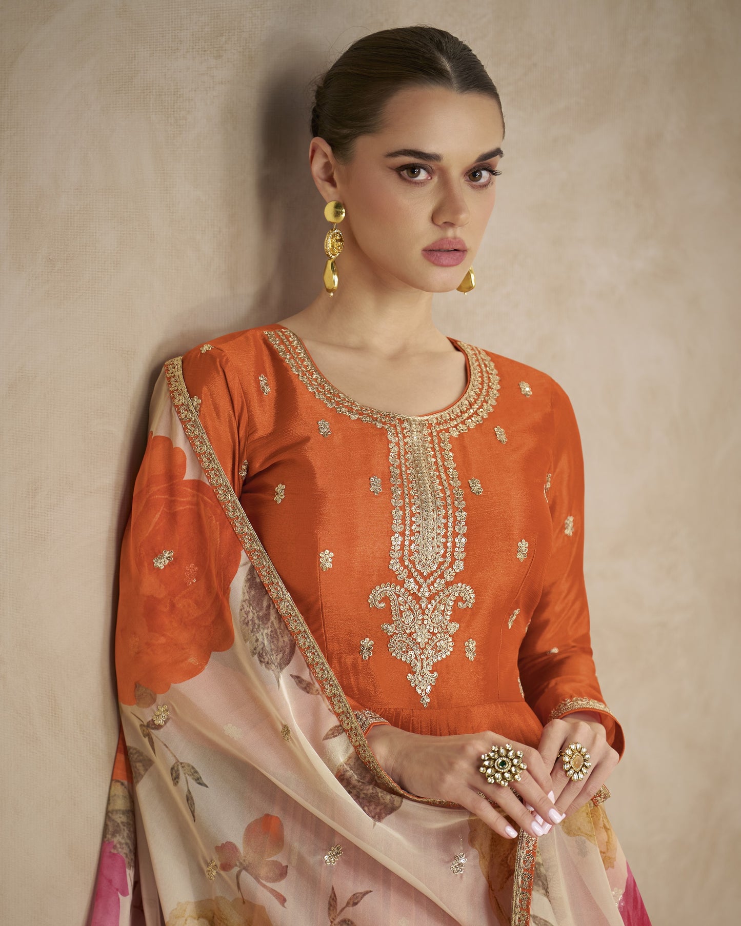 Woman wearing an orange embroidered traditional outfit with a beige background