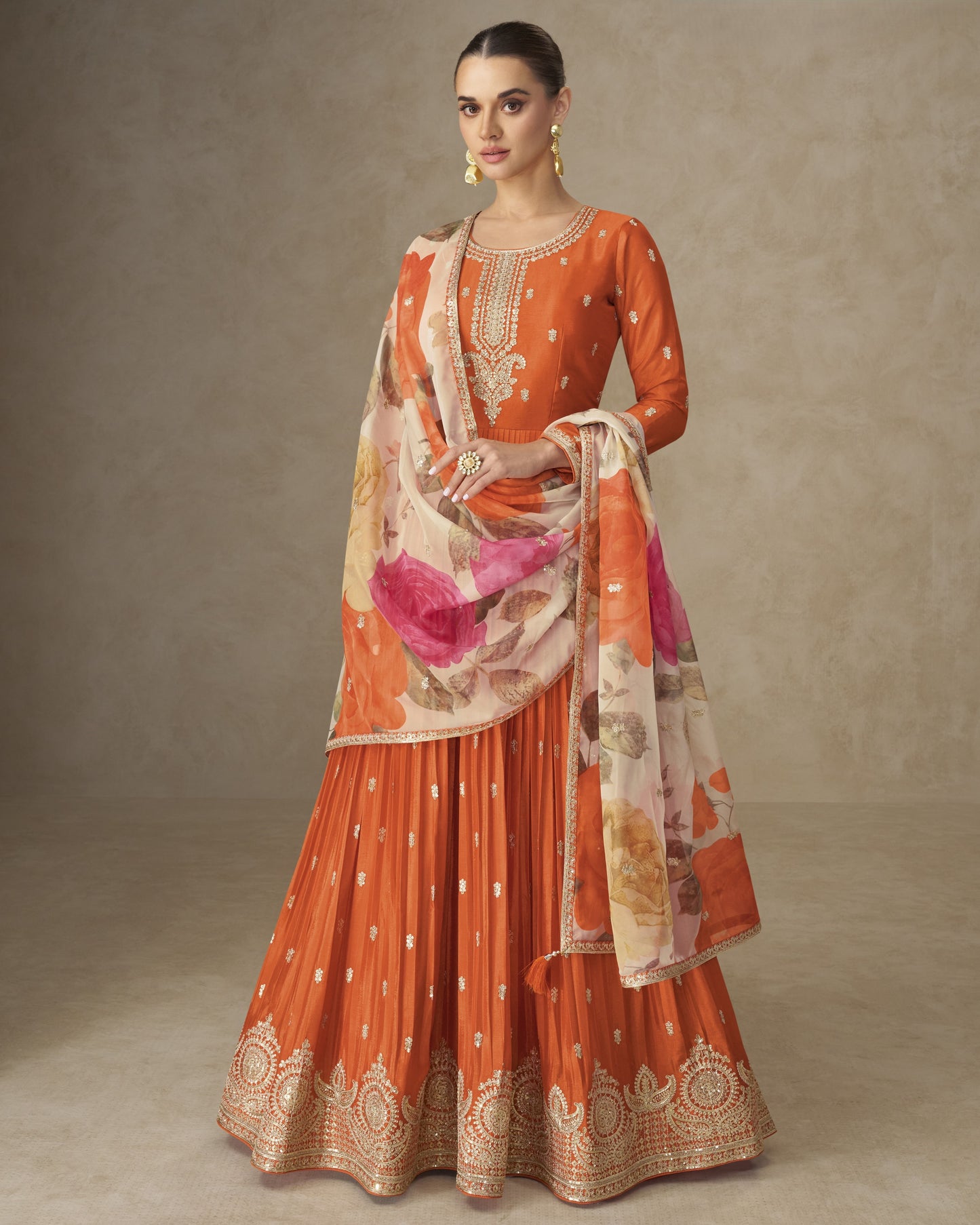 Woman wearing an orange traditional outfit with a matching dupatta on a plain background